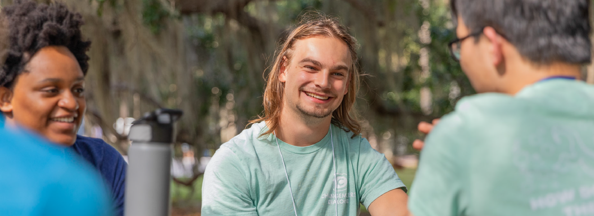 Three students talking while sitting at a picnic table outside.